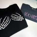 Black skeleton-hands sweatshirt and gray BOO-BIES shirt laid flat