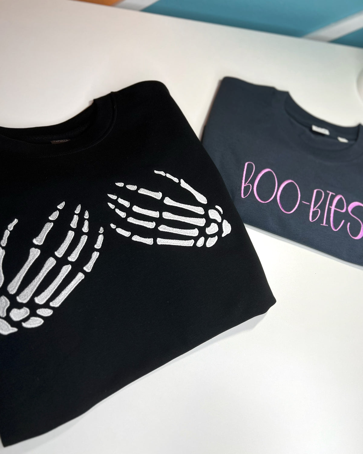 Black skeleton-hands sweatshirt and gray BOO-BIES shirt laid flat