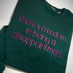 Green sweatshirt with pink There's Freedom in Being a Disappointment embroidery