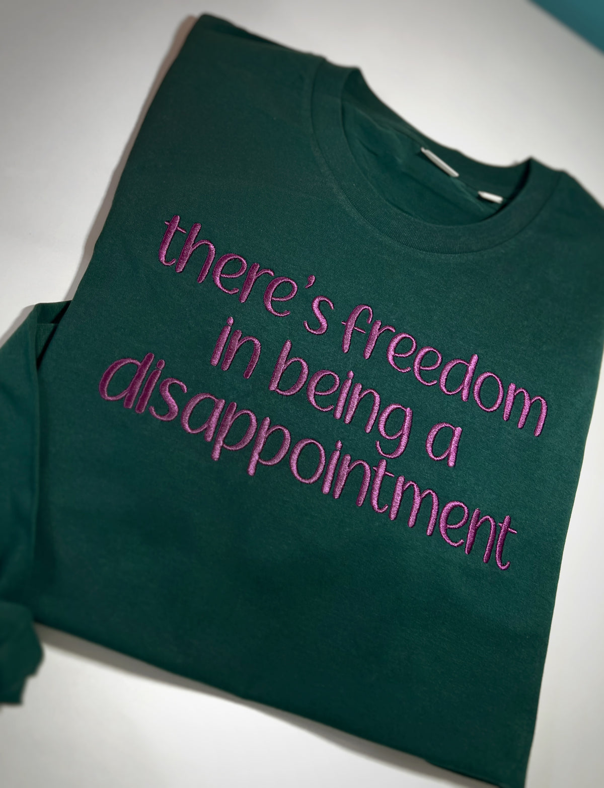 Green sweatshirt with pink There's Freedom in Being a Disappointment embroidery