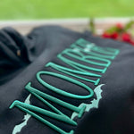 Close-up of raised green MOMBIE lettering on black fabric