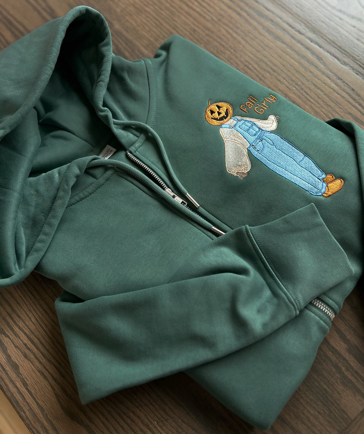Green zip-up hoodie with embroidered pumpkin-headed scarecrow