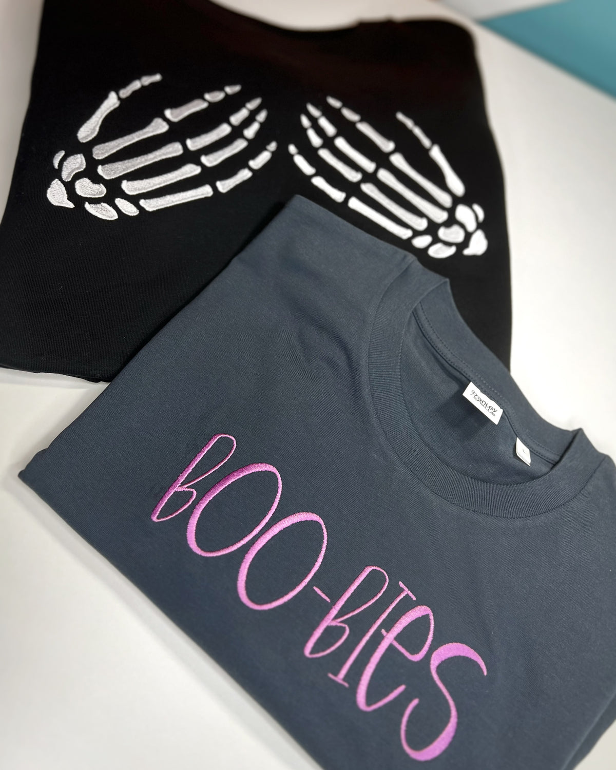 Black skeleton-hands sweatshirt beside gray BOO-BIES shirt