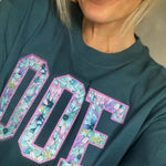 Person wearing a teal sweatshirt with floral OOF appliqué