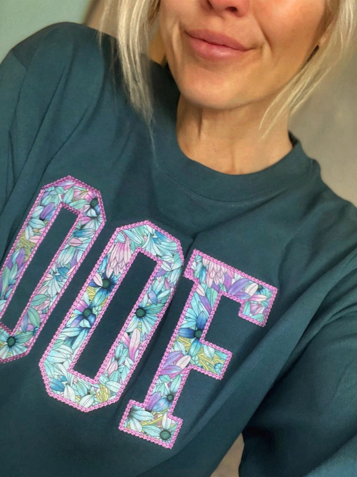 Person wearing a teal sweatshirt with floral OOF appliqué
