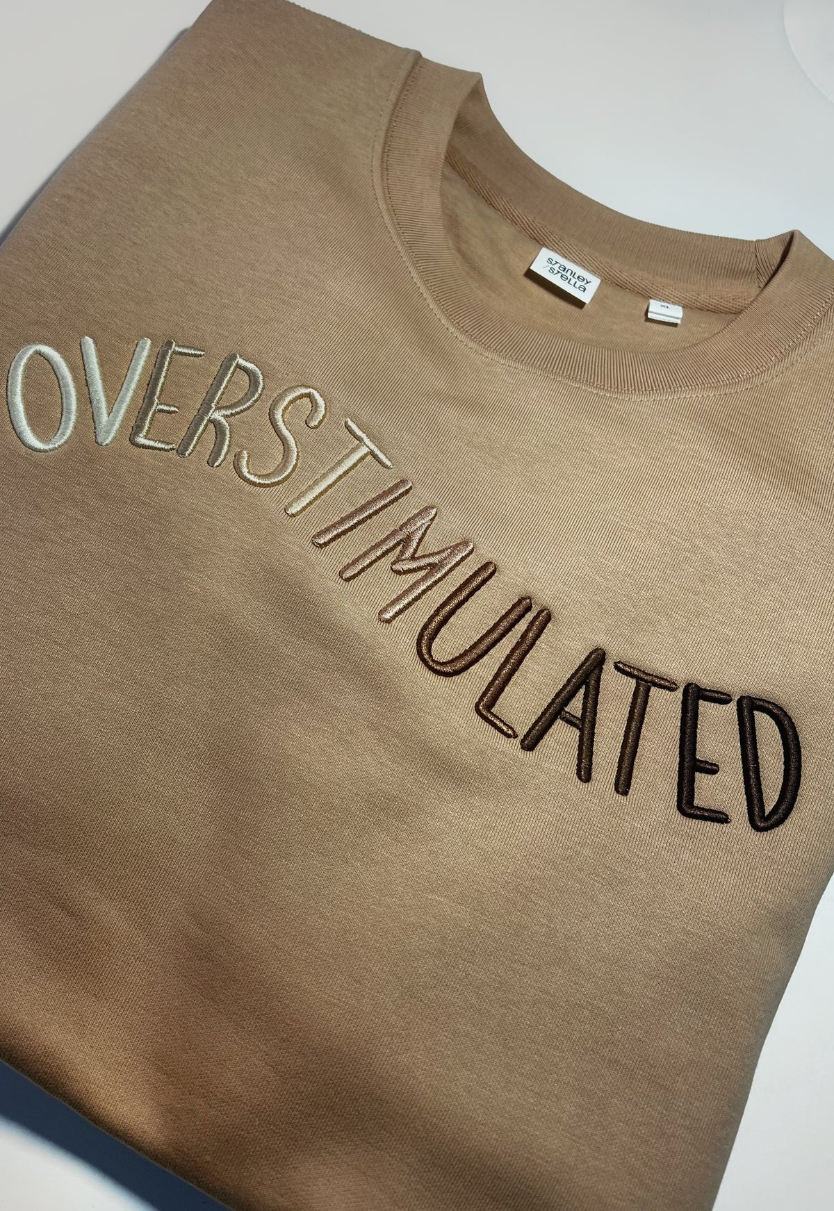 Tan sweatshirt with tonal OVERSTIMULATED puff embroidery