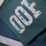 Folded teal OOF sweatshirt with floral fabric letters
