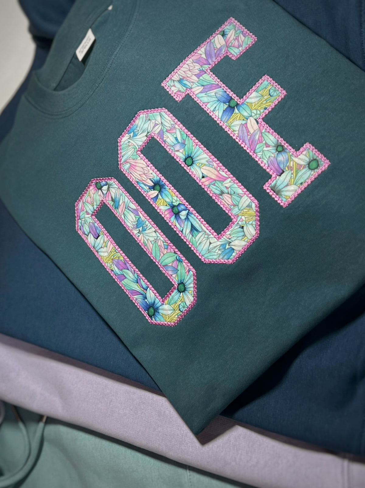 Folded teal OOF sweatshirt with floral fabric letters